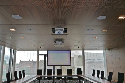 Konferenzraum mit gelochter Holzdecke, Beamer und Leinwand vor Fensterfront – Sparkasse Spree-Neiße, Cottbus