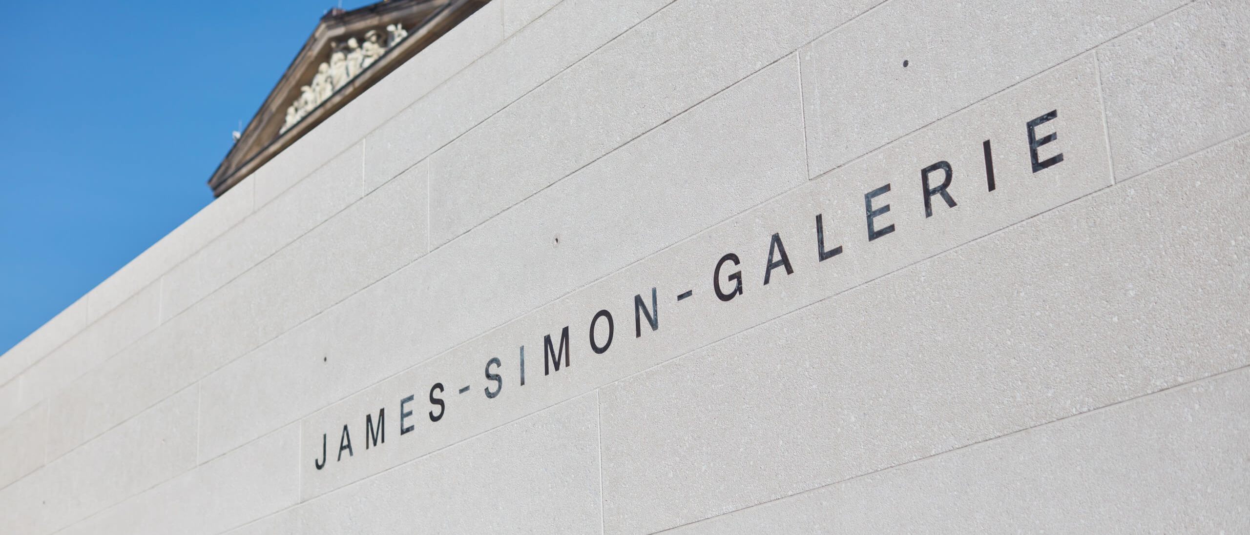 Detail des Schriftzugs auf der Natursteinwand vor blauem Himmel – James-Simon-Galerie, Berlin