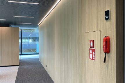 Flur mit Wandverkleidung in hellem Holzfurnier, Lamellendecke und LED-Lichtlinie – Mensa Würzburg