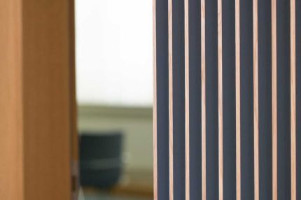 Detail der Holzlamellen an offener Tür, dahinter unscharf ein Büro mit Stuhl – MOZ-Areal VR-Bank, Würzburg