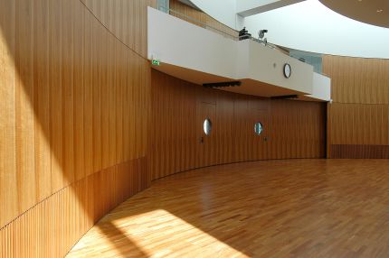 Leerer Saal mit gebogener Holz-Wandverkleidung und Bullaugentüren unter der Empore – IHK Potsdam