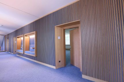 Flur mit offener Eichentür in der Lamellenwand und Sitznischen im Hintergrund – MOZ-Areal VR-Bank, Würzburg