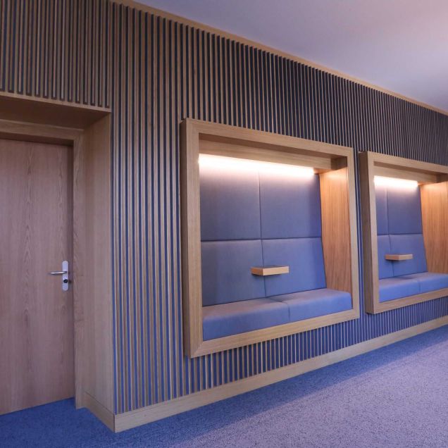 Zwei gepolsterte Sitznischen mit Lichtband in der Lamellenwand neben Eichentür – MOZ-Areal VR-Bank, Würzburg
