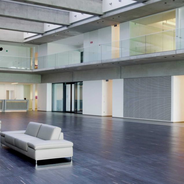 Atrium mit weißen Sofas, Galerie mit Glasbrüstung und Lamellenwand – Willy Naessens Group, Belgien