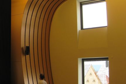 Bühne im Saal mit bis zum Boden geschwungener Holzlamellenverkleidung – Bürgerhaus Lechner Bräu