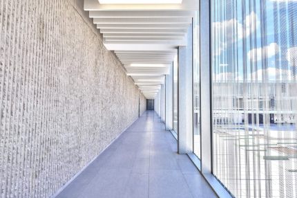 Langer Flur zwischen gerillter Betonwand und Glasfassade mit Lamellendecke – Gymnasium Oberursel