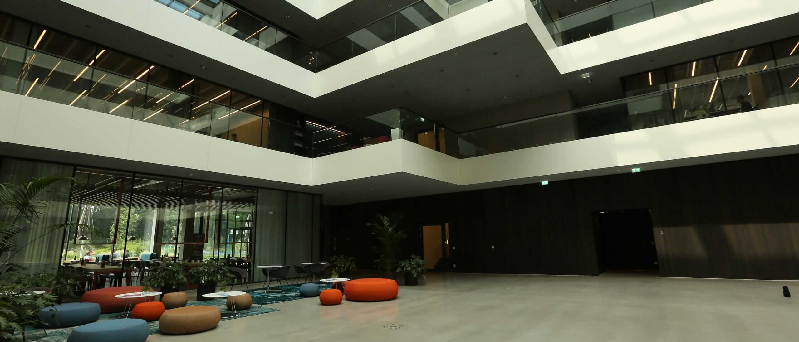 Lichthof mit farbigen Sitzpoufs und dunkler Holzwandverkleidung im Erdgeschoss – AEB-Zentrale, Stuttgart