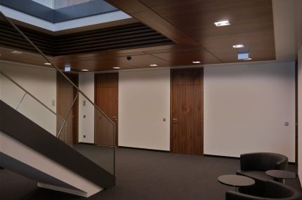 Treppenhalle mit Nussbaum-Decke, Holzlamellen am Oberlicht und Holztüren – Sparkasse Spree-Neiße, Cottbus