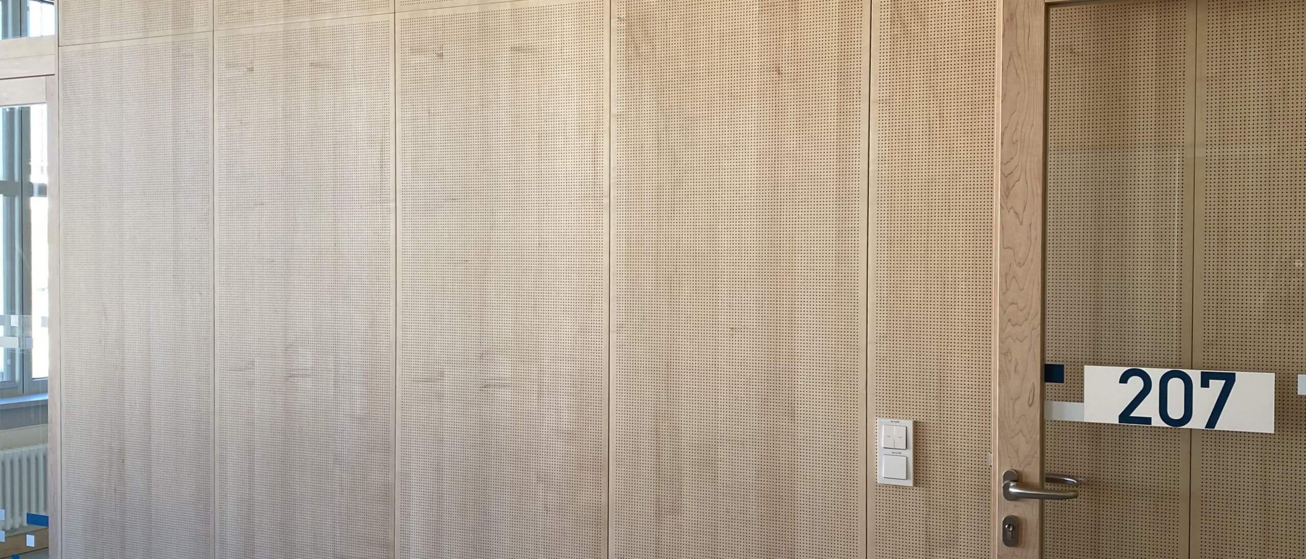 Detail der gelochten Holz-Wandverkleidung mit Tür zu Raum 207 – Bildungskampus Köln