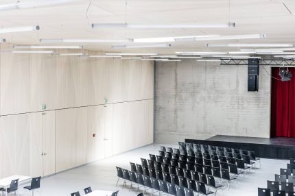 Saal mit Bühne, rotem Vorhang und heller Holz-Wandverkleidung mit integrierten Türen – Gymnasium Oberursel