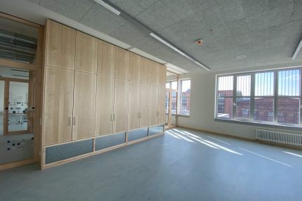 Klassenraum mit Einbauschrank aus Holz, Akustikdecke und großen Fenstern – Bildungskampus Köln