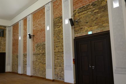 Saalwand mit Sichtmauerwerk, Pilastern, Lautsprechern und Holztür – Neues Schloss Bad Muskau