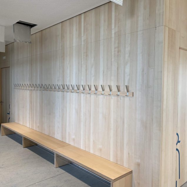 Flur mit Holz-Wandverkleidung, Garderobenhaken, Sitzbank und Akustikdecke – Bildungskampus Köln
