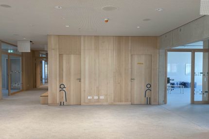 Flurzone mit holzverkleidetem Sanitärblock und Lochdecke – Bildungskampus Köln