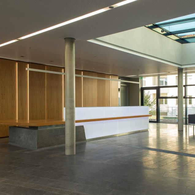 Foyer mit Empfangstheke, Holz-Wandverkleidung, Lochplattendecke und Oberlicht – Deutsche Rentenversicherung, Würzburg