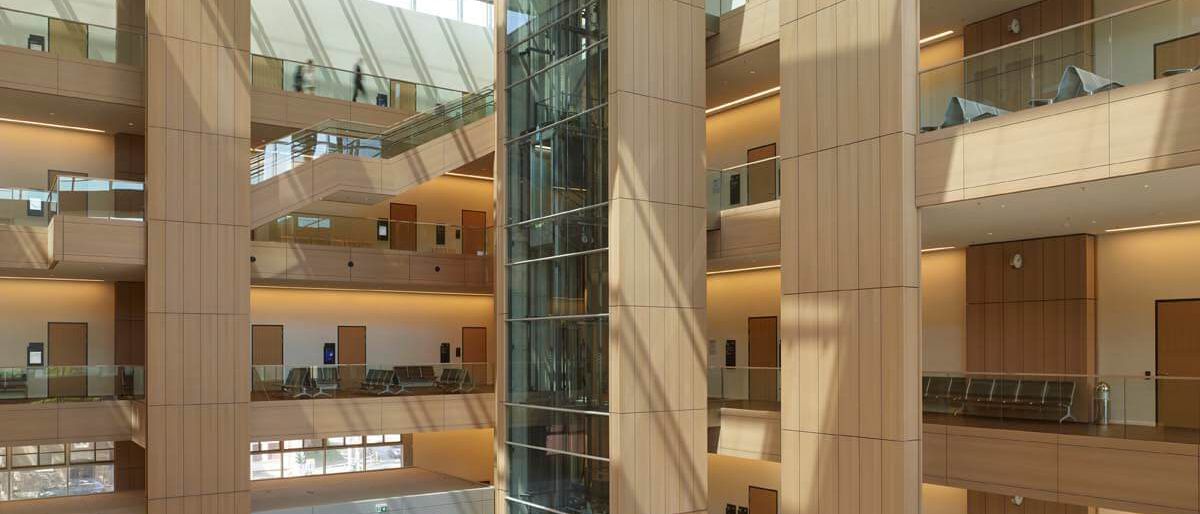 Lichthof mit Informationstheke, holzverkleideten Pfeilern und gläsernem Aufzug – Justizzentrum Bochum