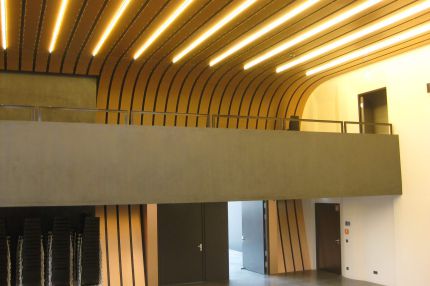 Saal mit Empore unter geschwungener Lamellendecke und gestapelten Stühlen – Bürgerhaus Lechner Bräu