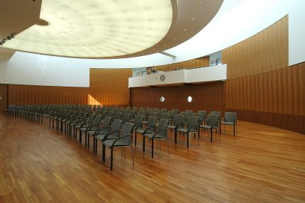 Saal mit geschwungener Holz-Wandverkleidung und Stuhlreihen, Schrägansicht – IHK Potsdam