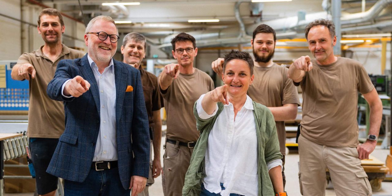 Eine Gruppe von Fachleuten lächelt und zeigt auf die Kamera in einem Workshop für akustische Lösungen und Wandverkleidungen.